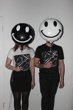 two people standing next to each other with balloons in the shape of smiley faces on their heads