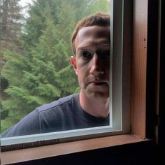 a man looking through a window with trees in the background