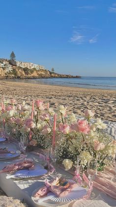 a table set up on the beach with flowers and candles