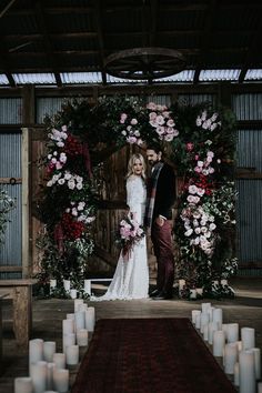 a bride and groom standing in front of a floral arch with candles on the floor