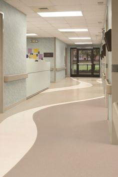 an empty hospital hallway with white walls and beige flooring, along with large windows