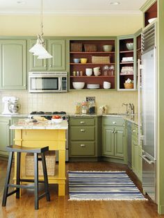 a kitchen with green cabinets and white counter tops, along with a yellow island in the middle