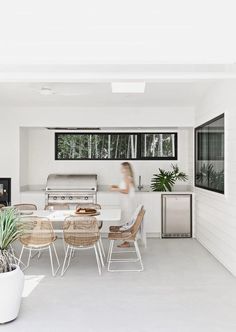 a woman standing in the kitchen next to a table with chairs and potted plants