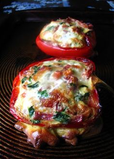 two stuffed red peppers sitting on top of a black plate with cheese and spinach