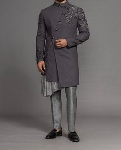 Grey IndoWestern Sherwani made of luxury suiting fabric with hand embroidered with cutdana stone and sequence work Suit has mandarin collar and long sleeves with a full button placket with overlapping placket that comes with a frill on slit asymmetrical hem and multiple slits and angrakha design that's overlaps asymmetrically over the chest middle chest  Comes with modern boot cut style pants with hook and zip closure and two side pockets   Size  Slim fit  Model height is 6 fit and wearing 40 si Indo Western Men Outfits, Sangeet Outfit For Men Indian Groom, Sherwani For Engagement, Mens Indowestern Outfits Wedding, Indowestern Outfits Wedding, Angrakha Design, Indo Western Menswear, Sangeet Outfit For Men, Indowestern Outfits For Men