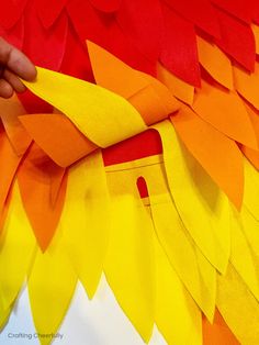 someone is making a paper bird out of strips of red and yellow material with scissors