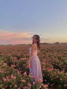 a woman standing in the middle of a field full of flowers at sunset or dawn