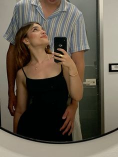 a woman looking at her cell phone while standing in front of a man taking a selfie