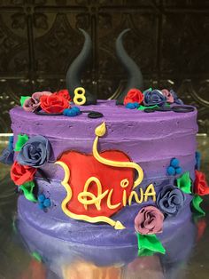 there is a purple cake decorated with flowers and an elephant on the top, surrounded by devil horns