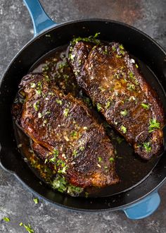 two steaks cooking in a skillet with herbs on the side and seasoning