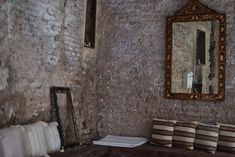 an old room with a mirror and some pillows on the bench in front of it