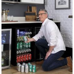 a man kneeling down in front of an open refrigerator filled with sodas and cans