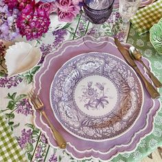 the table is set with plates, silverware and purple flowers in vases on it