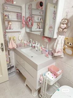 a white bathroom with pink accessories on the vanity and teddy bears hanging from the wall