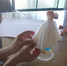 someone is holding a paper towel over a plastic cup on top of a wooden table