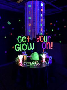 a table topped with lots of cake and cupcakes next to a neon sign that says get your glow on