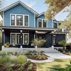 a blue house with lots of windows and plants on the front lawn in front of it