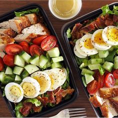 two trays filled with different types of food on top of a wooden table next to silverware