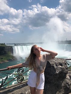 a woman standing in front of a waterfall with her hands on her head and arms behind her head