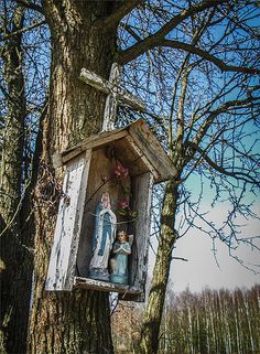 an old wooden birdhouse hanging from a tree in the woods with statues on it