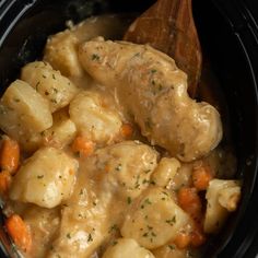 a crock pot filled with chicken and carrots next to a wooden ladle