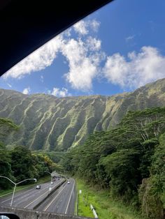 the view from inside a vehicle looking at mountains and trees on either side of the road