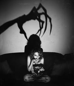 a woman sitting on top of a couch next to a shadow of a person holding a cake