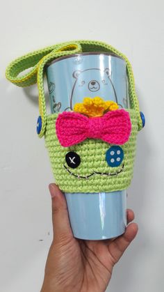 a hand holding a cup with a bear on it and a bow tie around its neck