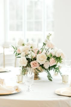 a table with white and pink flowers in a vase on top of it next to silverware