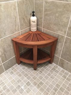 a wooden shelf in the corner of a tiled shower stall with a bottle on top