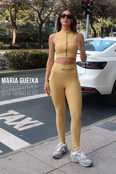 a woman standing on the sidewalk in her yellow sports bra and matching leggings