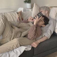 two people laying on a couch looking at a cell phone and taking a selfie