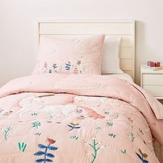 a bed with pink comforter and pillows on top of it next to a night stand