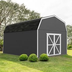 a large gray barn sitting on top of a lush green field next to some trees