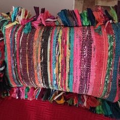 a multicolored striped pillow sitting on top of a red bed cover next to a wooden headboard