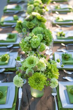 a long table is set with green and white plates, silverware, and flowers