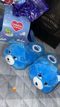 two blue teddy bears sitting on top of a bed next to a bag and some candy