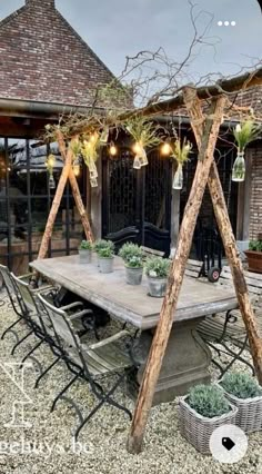 an outdoor dining area with potted plants on the table and lights hanging from the roof