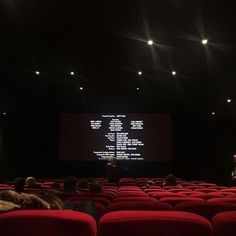 people sitting on red chairs in front of a projector screen with words projected on it