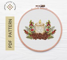 a cross stitch pattern with a candle and pine cones