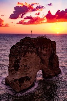 the sun is setting over an ocean with a rock formation