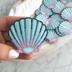 a hand holding a small blue and pink scallop shell brooch on a white plate