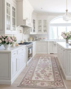 a kitchen with white cabinets and pink flowers in vases on the counter top next to an area rug