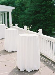 there are tables with white cloths on the outside patio and trees in the background