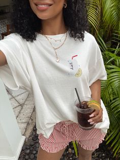 a woman holding a drink in her right hand and wearing a white t - shirt