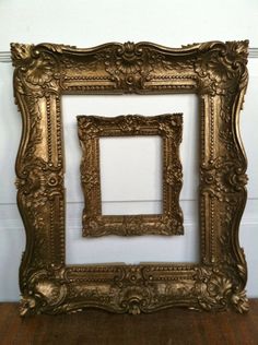 an ornate gold frame sitting on top of a wooden floor next to a white wall