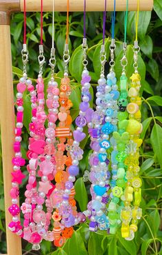 several different colored beads hanging from a wooden rack in front of plants and bushes with green leaves behind them