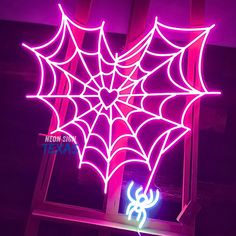 a spider web neon sign is lit up in the dark with purple lighting behind it