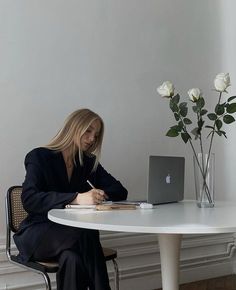 a woman sitting at a white table with a laptop and flowers in front of her