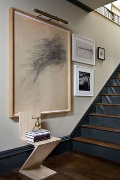 an art work hangs on the wall next to a stair case with books and magazines